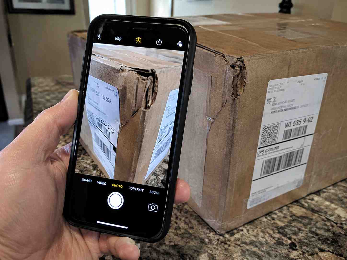 Close-up of a smartphone camera photographing a damaged corner of a cardboard shipping box and its label